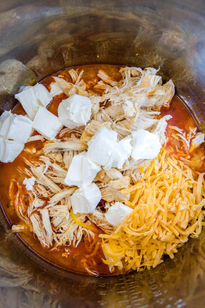 adding cheese and cream cheese to Instant pot of cooked chicken