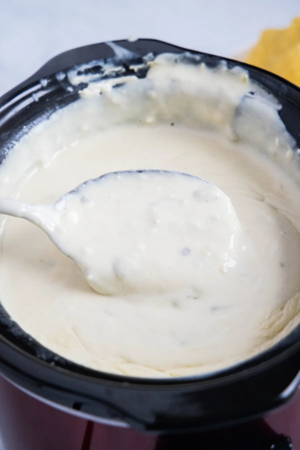 A serving spoon full of white queso dip, above a crock pot full of queso