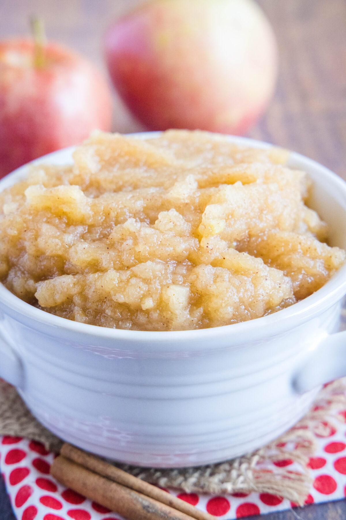 A bowl of applesauce with two apples in the background