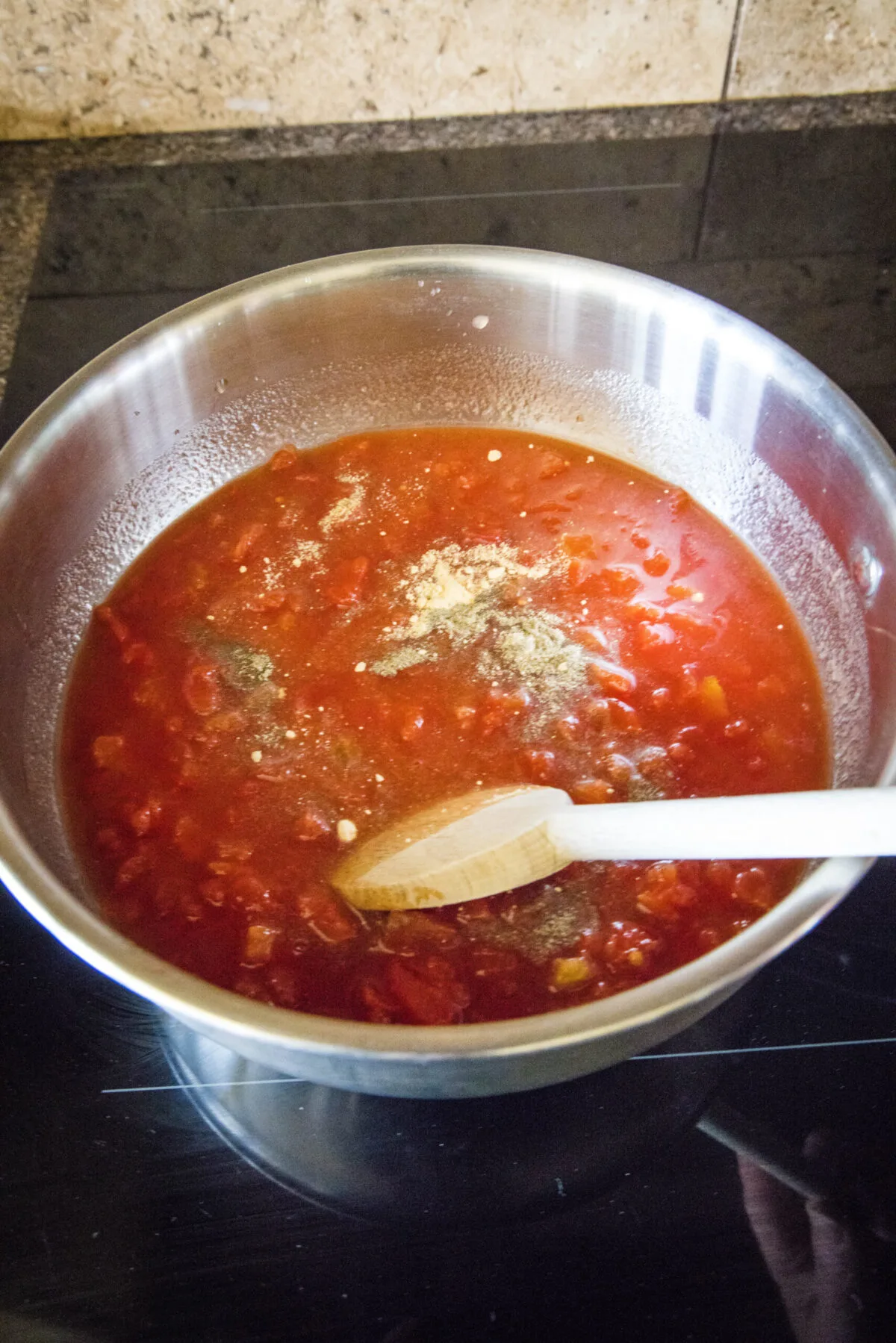 A wooden spoon stirring tomatoes, vinegar, and seasonings in a pot