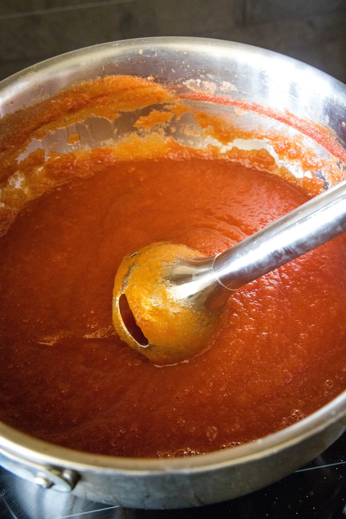 A stick blender blending ketchup in a pot