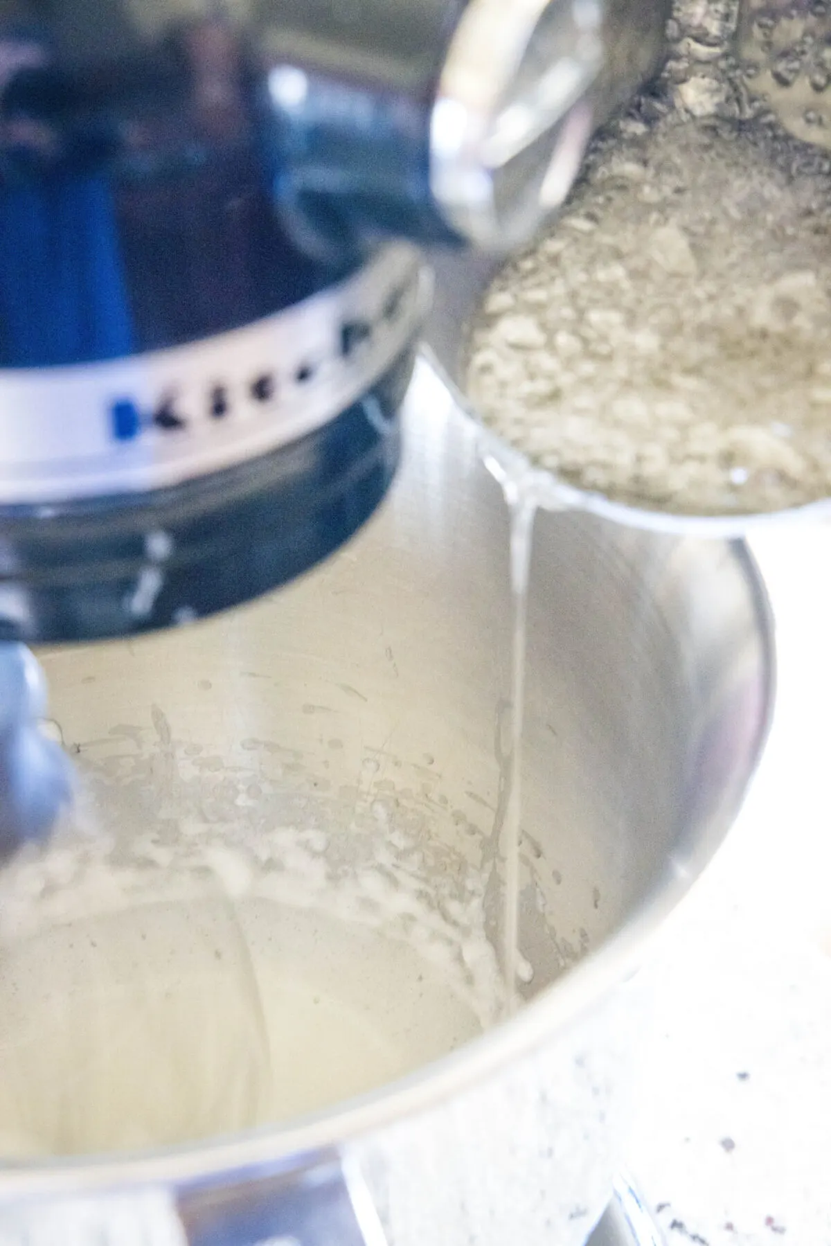 Boiling sugar being poured into beat egg whites in a stand mixer