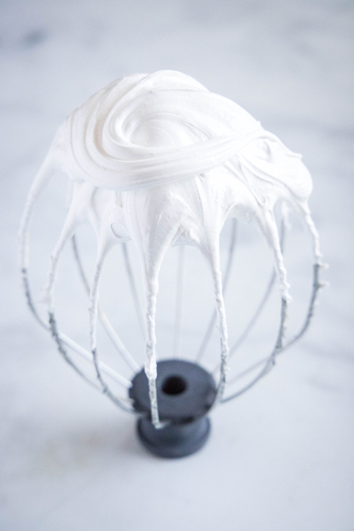 Close up of a stand mixer whisk attachment with soft peaks of egg whites