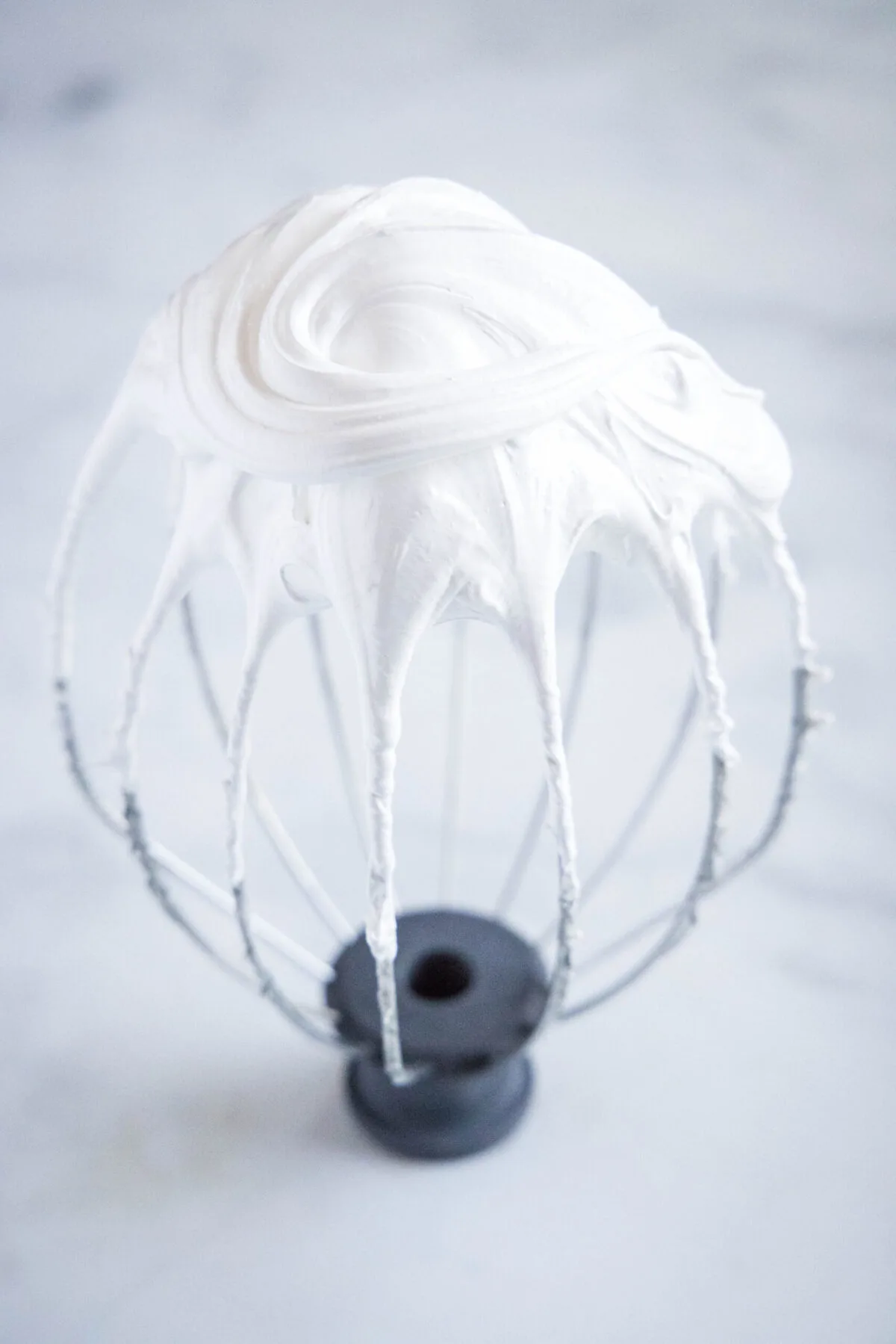 Close up of a stand mixer whisk attachment with soft peaks of egg whites