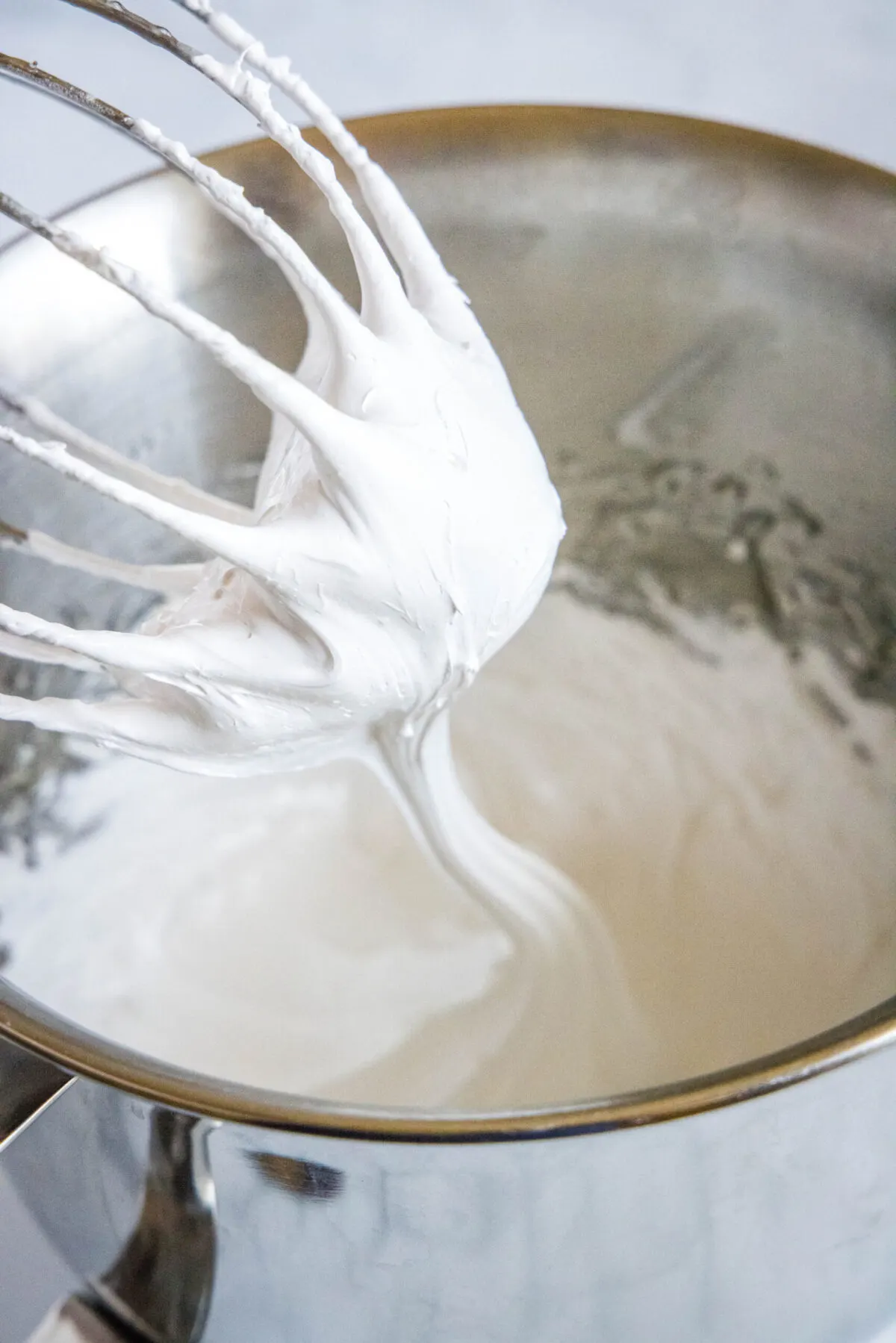 A stand mixer whisk attachment being pulled out of bowl filled with marshmallow fluff