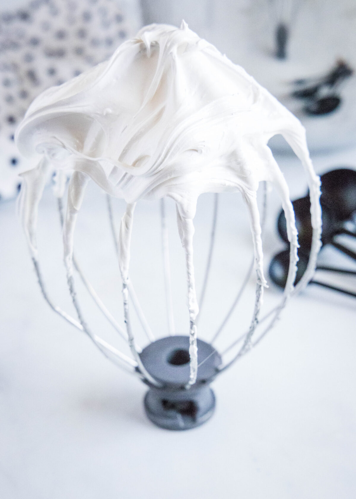 Close up of a stand mixer whisk attachment covered in stiff peaks of marshmallow fluff