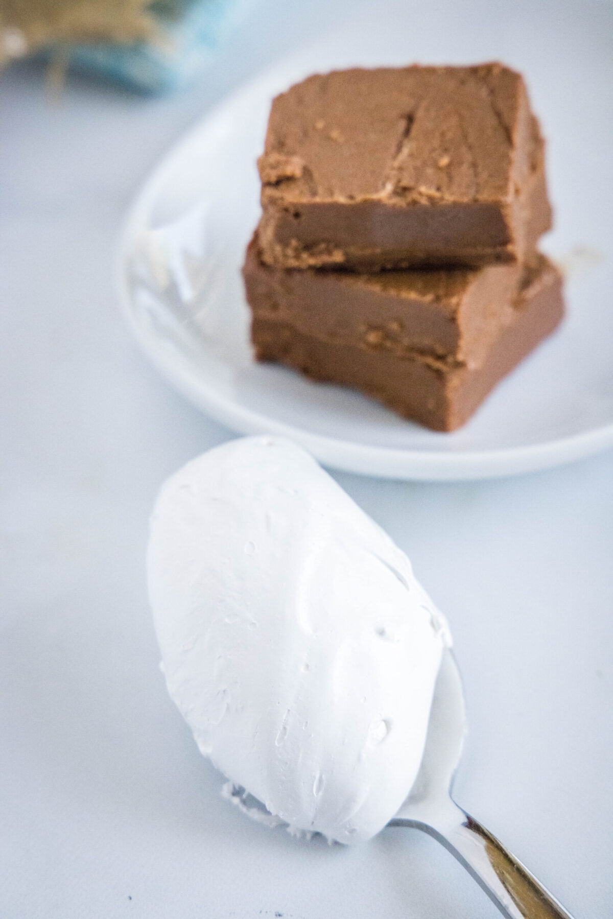A spoonful of marshmallow fluff next to a plate with two pieces of fudge