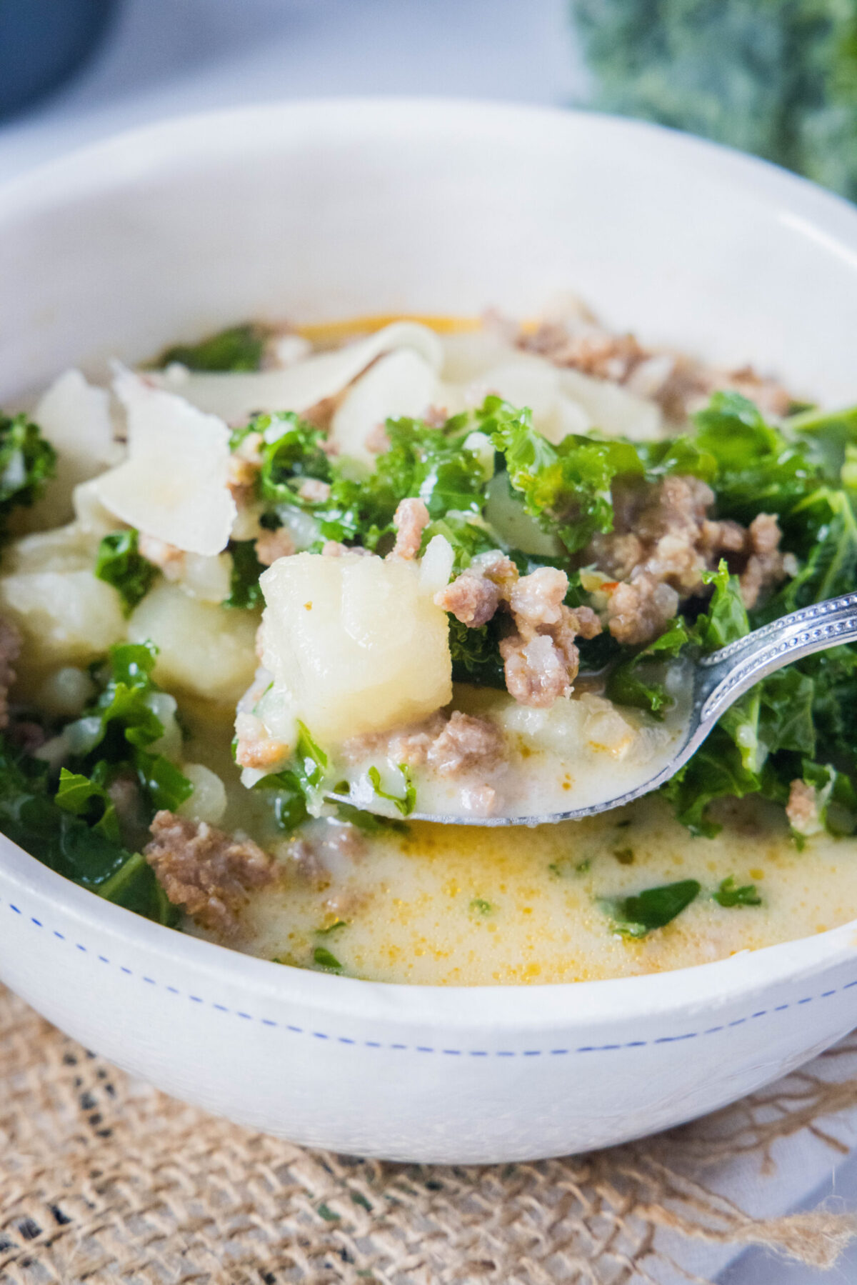 A bowl of Zuppa Toscana with a spoon taking a spoonful out
