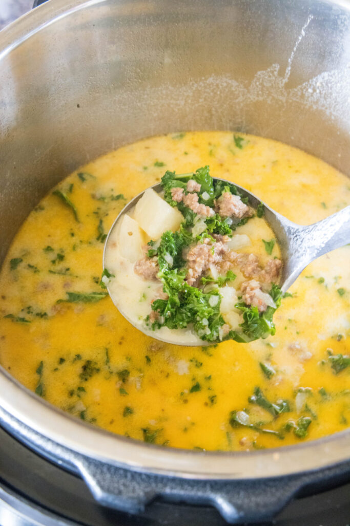 A ladle full of Zuppa Toscana with a pot full of it in the background
