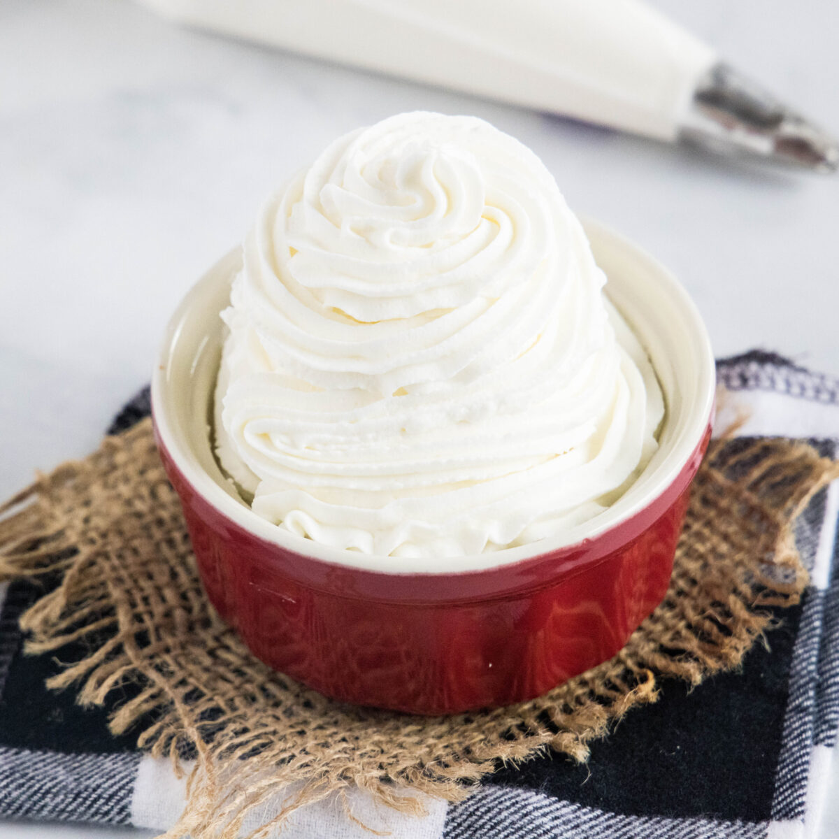 A ramekin of stabilized whipped cream, with a frosting piping bag in the background