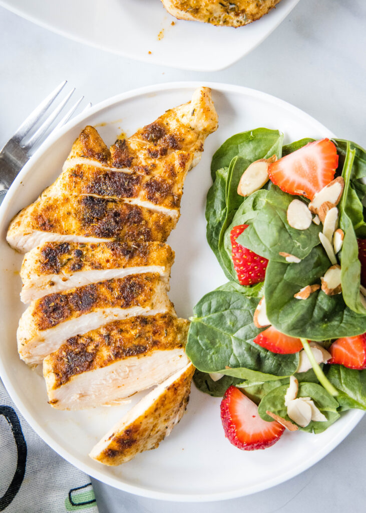 looking down on a plate with sliced blackened chicken and spinach salad