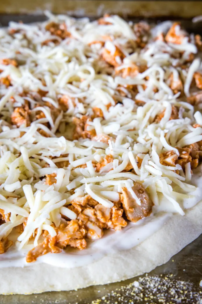 Unmelted cheese on top of buffalo chicken on top of ranch dressing on top of pizza dough