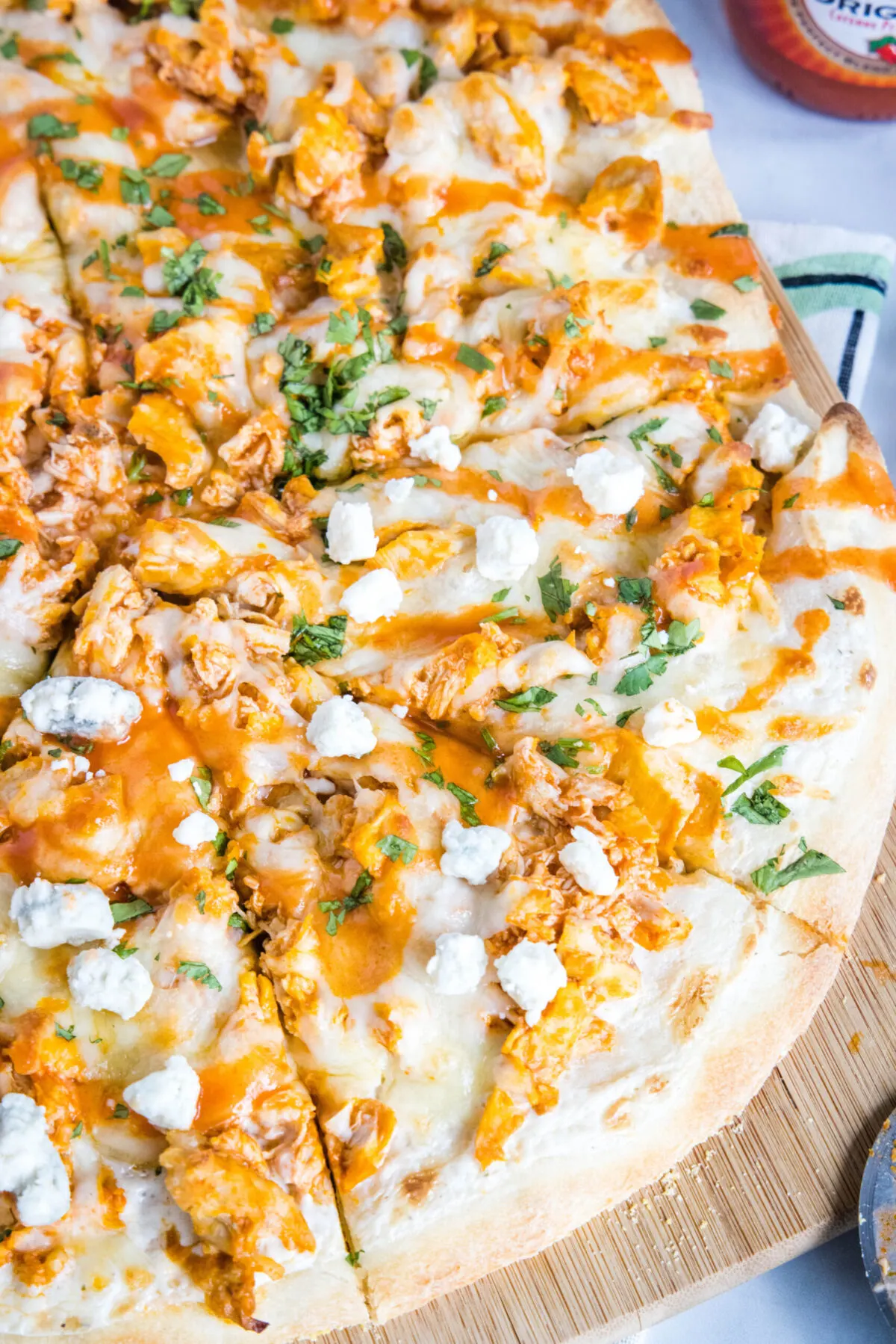Overhead view of buffalo chicken pizza topped with blue cheese and parsley, cut into slices