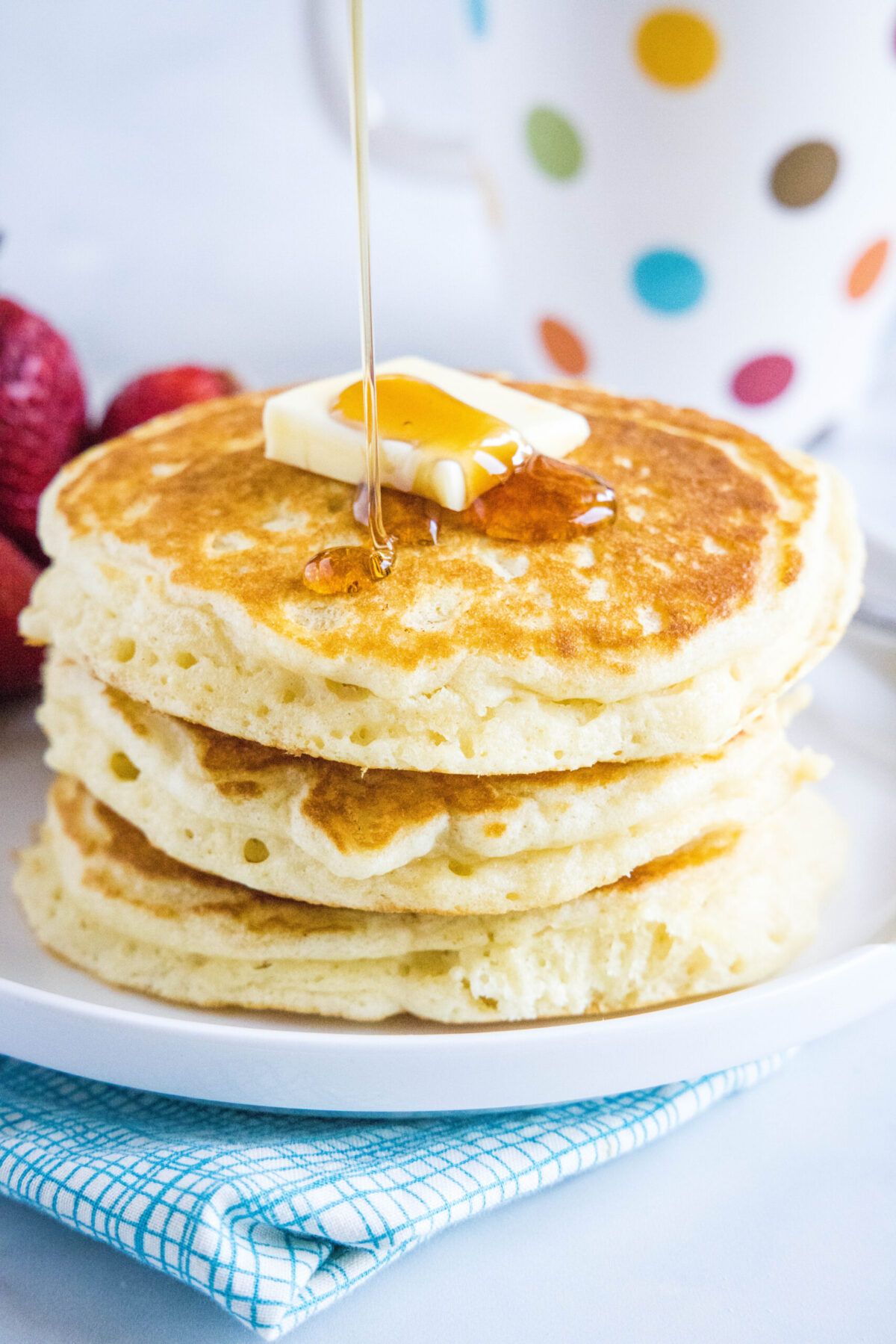 Syrup being poured onto a stack of pancakes that's topped with butter
