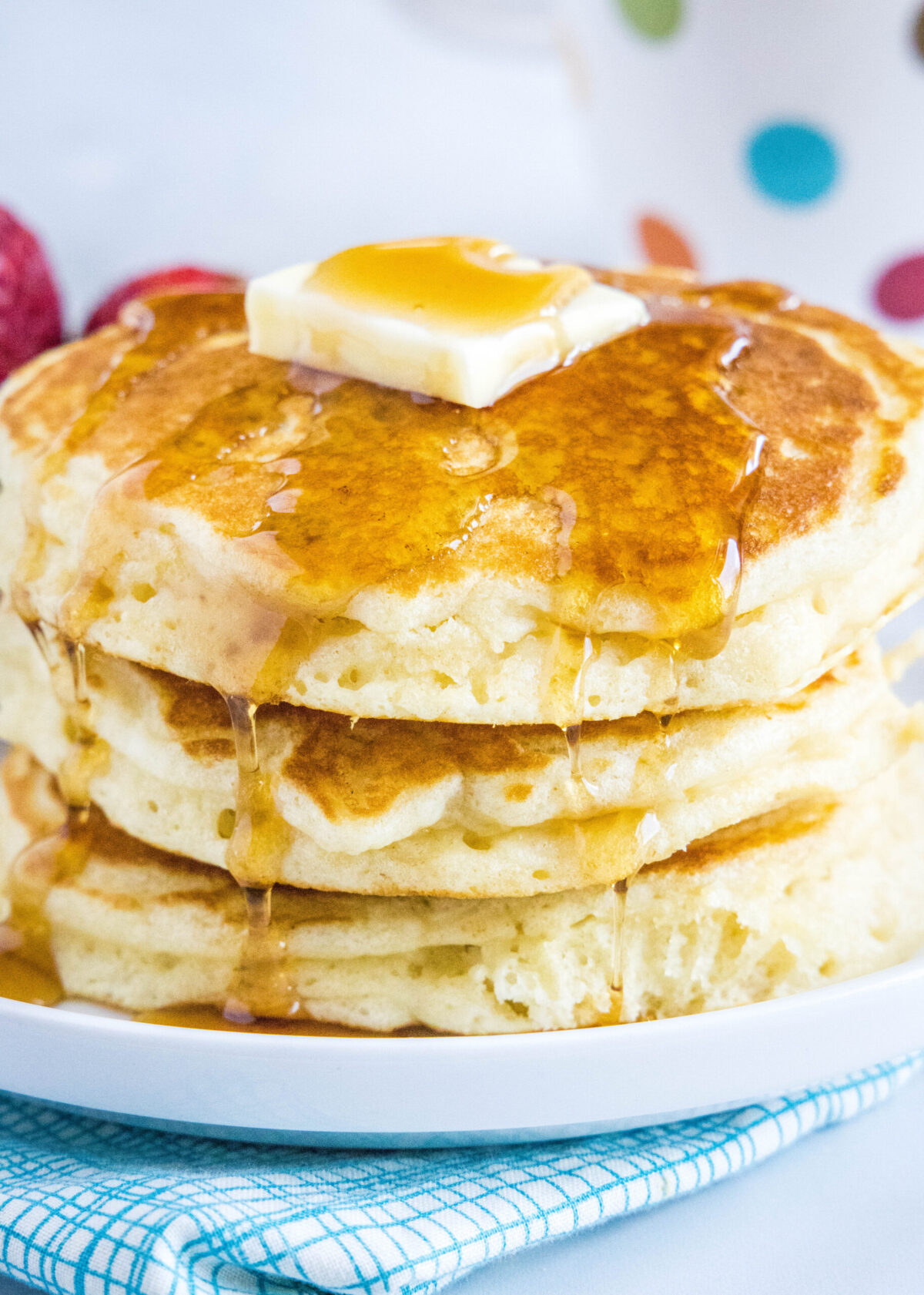 Close up of a stack of pancakes topped with butter and syrup