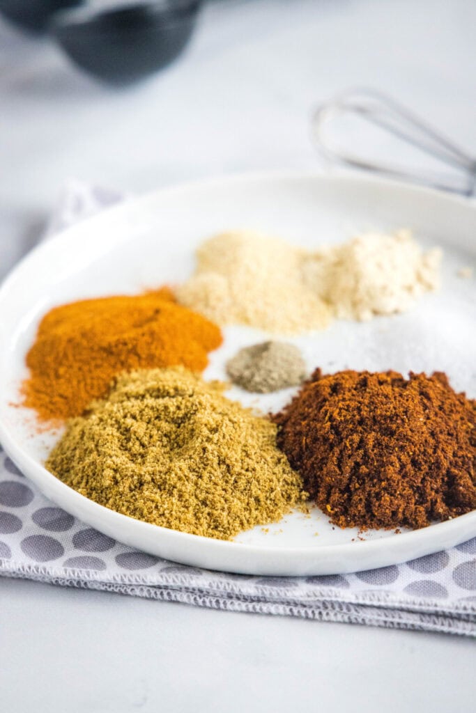 A round plate with piles of salt, pepper, garlic powder, onion powder, paprika, ground cumin, and chili powder