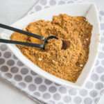 A white triangular bowl filled with fajita seasoning with a serving spoon