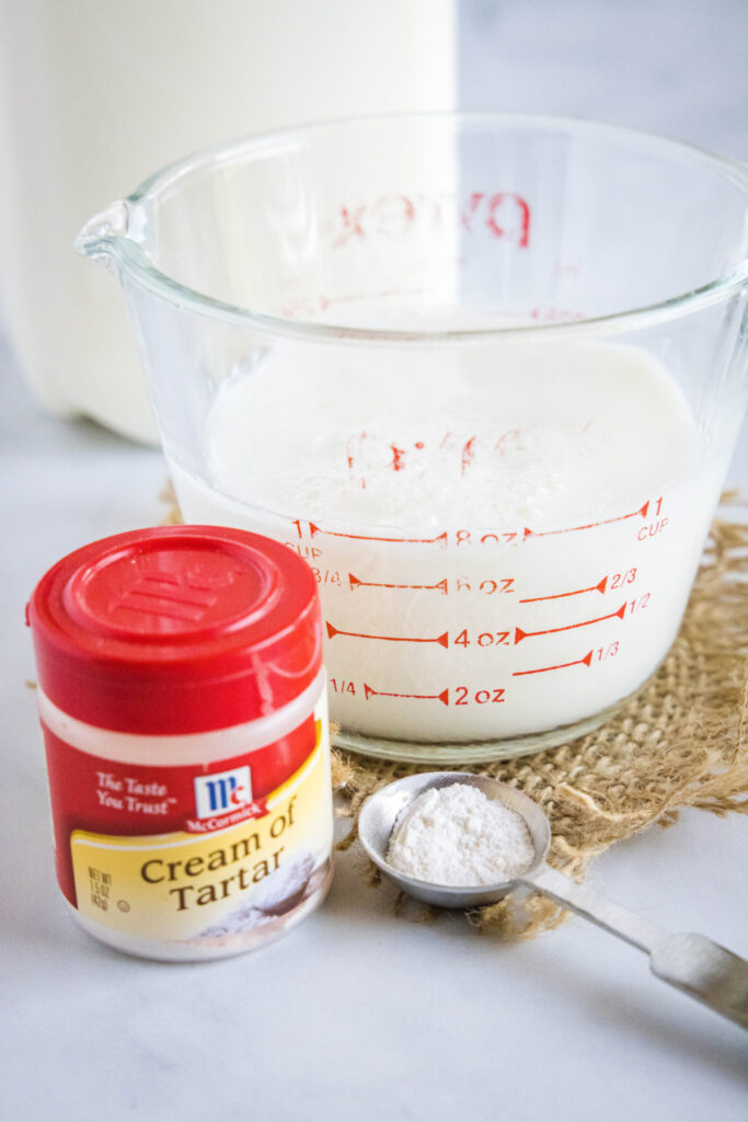 A pyrex filled with milk, a bottle of milk, a container of cream of tartar, and a measuring spoon with cream of tartar in it