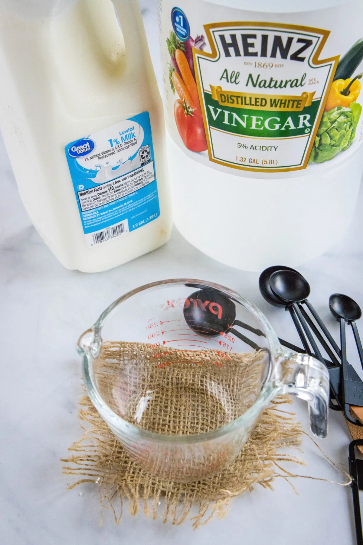 Overhead view of the ingredients needed for homemade buttermilk: a bottle of distilled vinegar, a carton of milk, a measuring cup, and measuring spoons