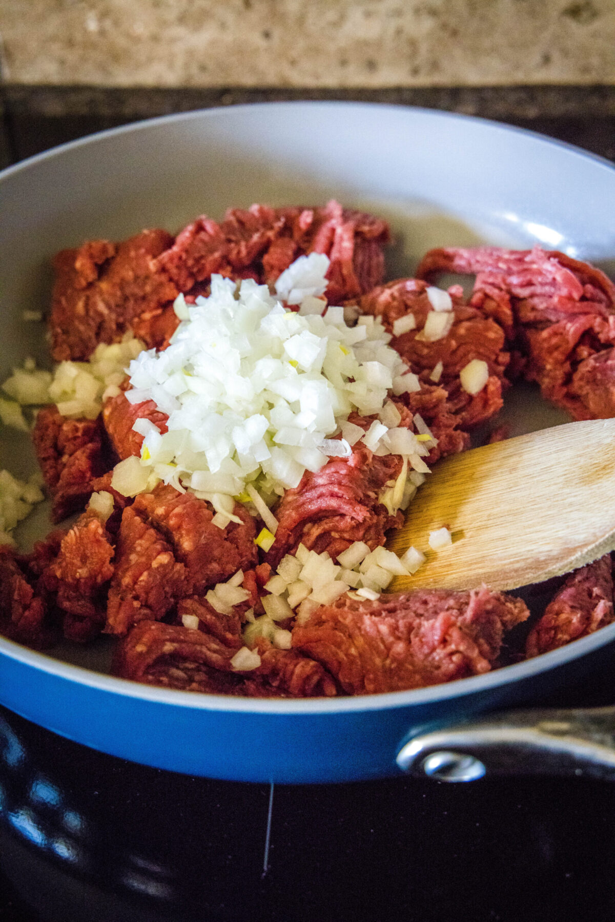 Raw beef and onions being mixed together in a skillet