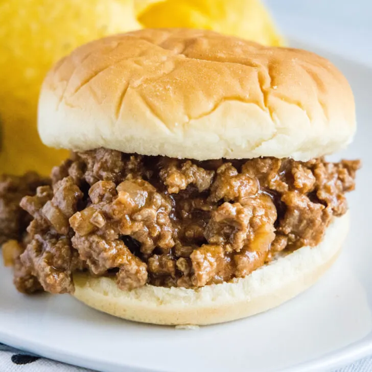 Close up of a sloppy joe sandwich on a plate with chips