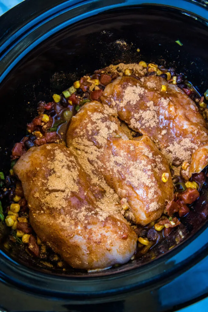 Seasoned chicken breasts on top of veggies and beans in a crock pot