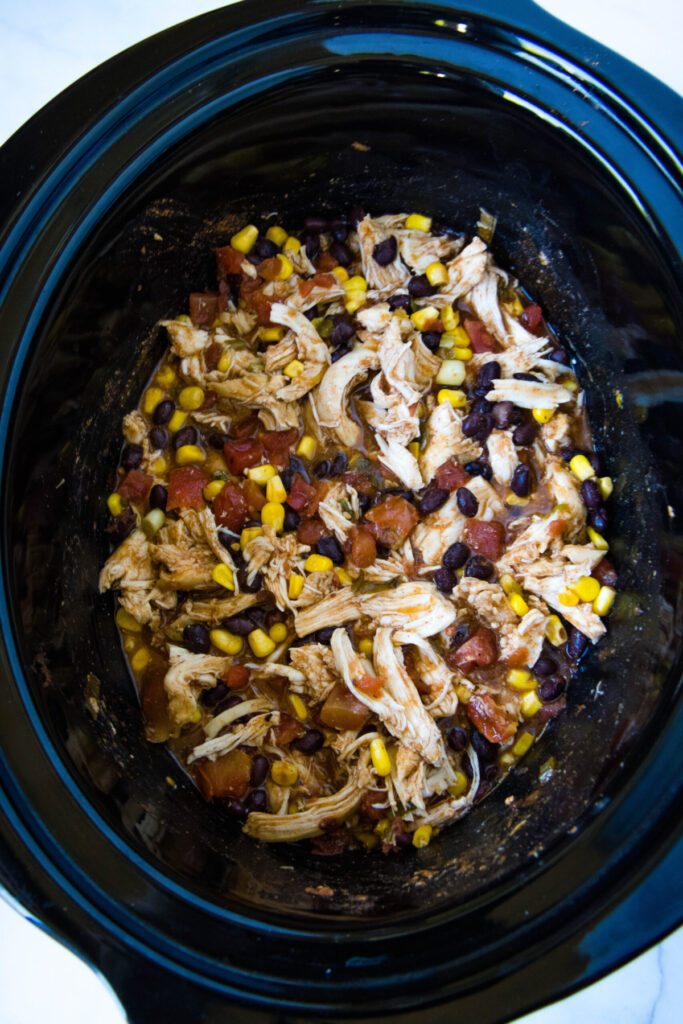 Overhead view of shredded chicken in a crockpot with corn, tomatoes, and beans