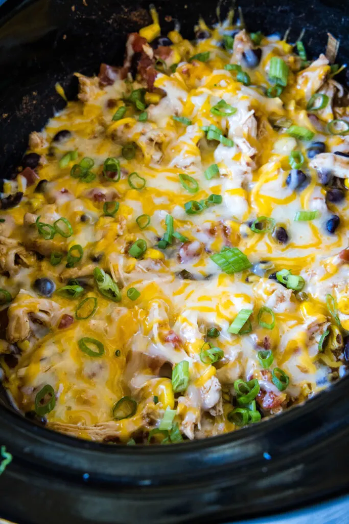 Overhead view of a crock pot full of Santa Fe chicken, topped with melted cheese and green onions