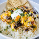 Close up of a bowl of rice with southwest chicken on top, topped with sour cream and green onions, with tortilla chips