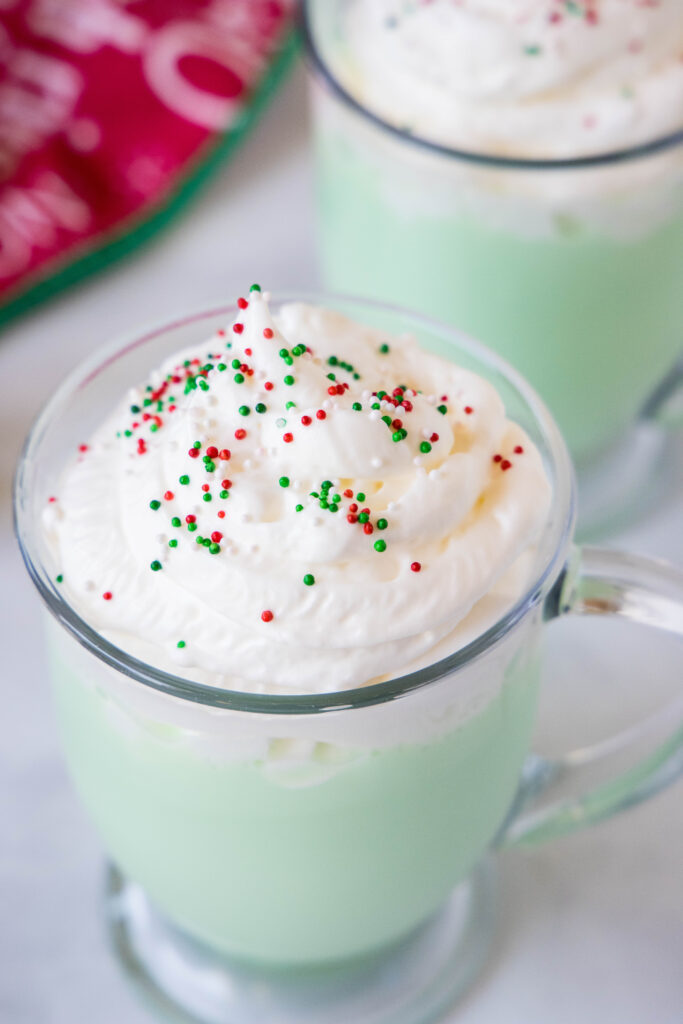 peppermint white hot chocolate in a mug with whipped cream and christmas sprinkles
