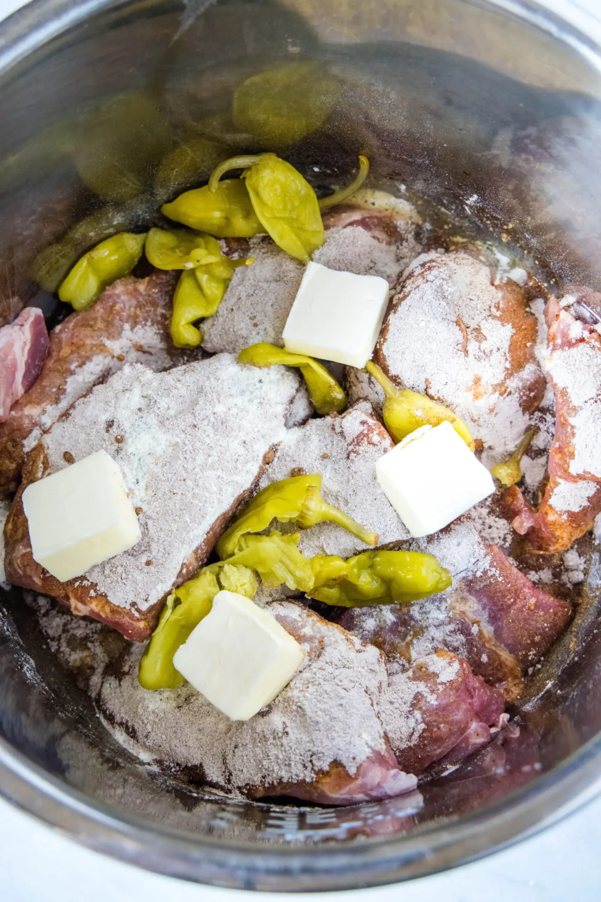 Raw pork in an Instant pot covered with seasoning, pepperoncini peppers, and pieces of butter