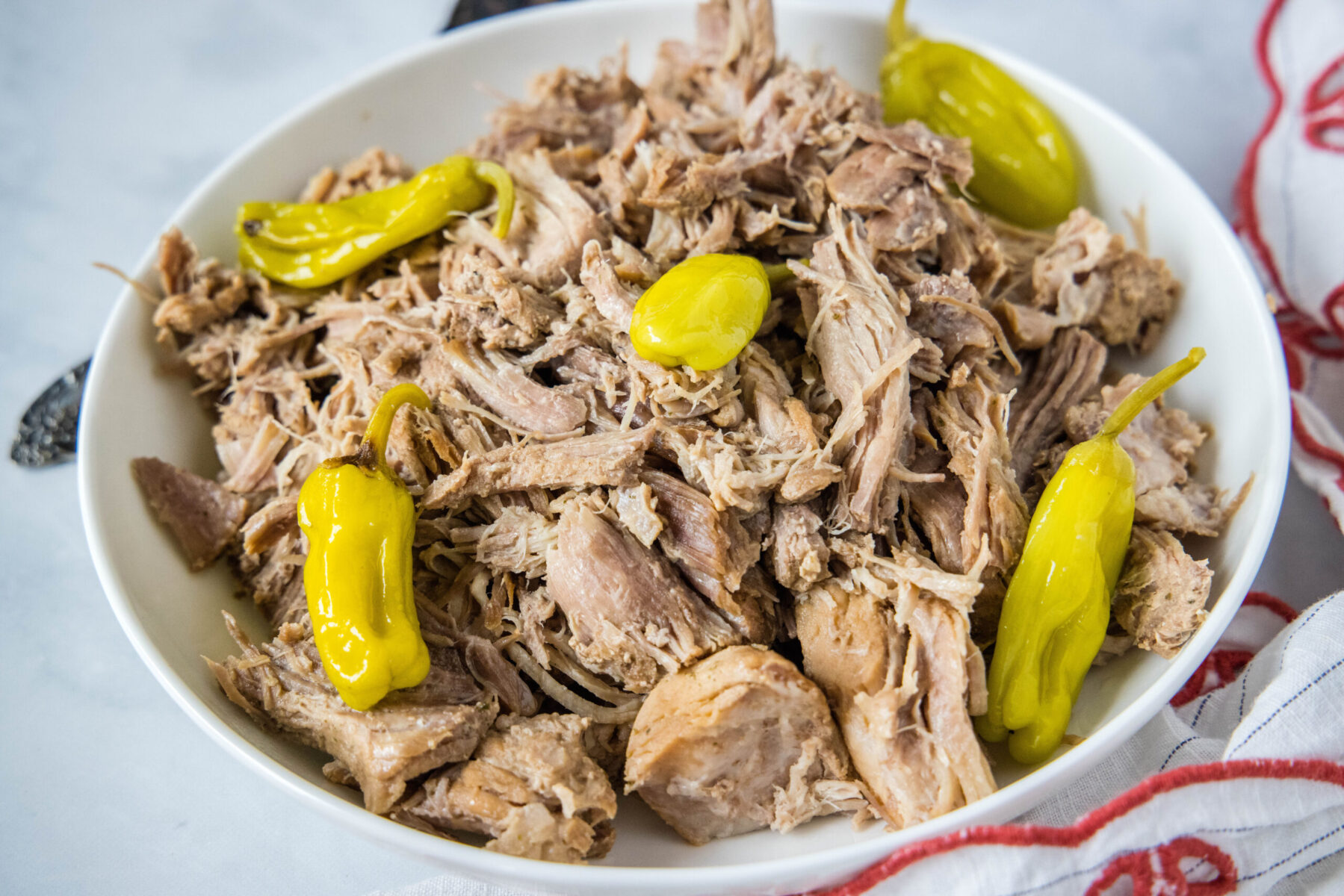 A bowl full of shredded pork with pepperoncini peppers