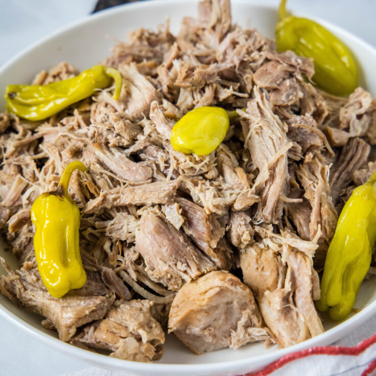 A bowl of shredded pork topped with pepperoncini peppers