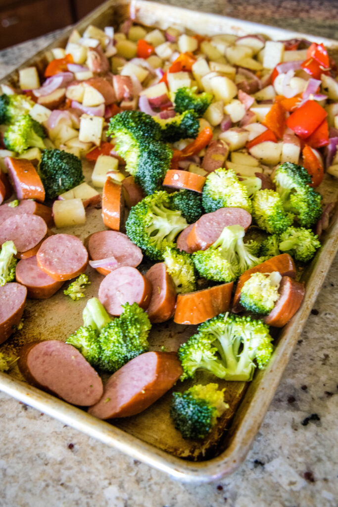 adding sausage and broccoli to the baking tray