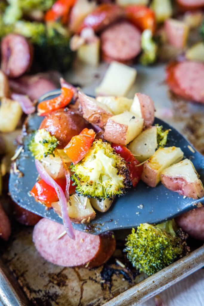 using a spatula to scoop up roasted potatoes and vegetables