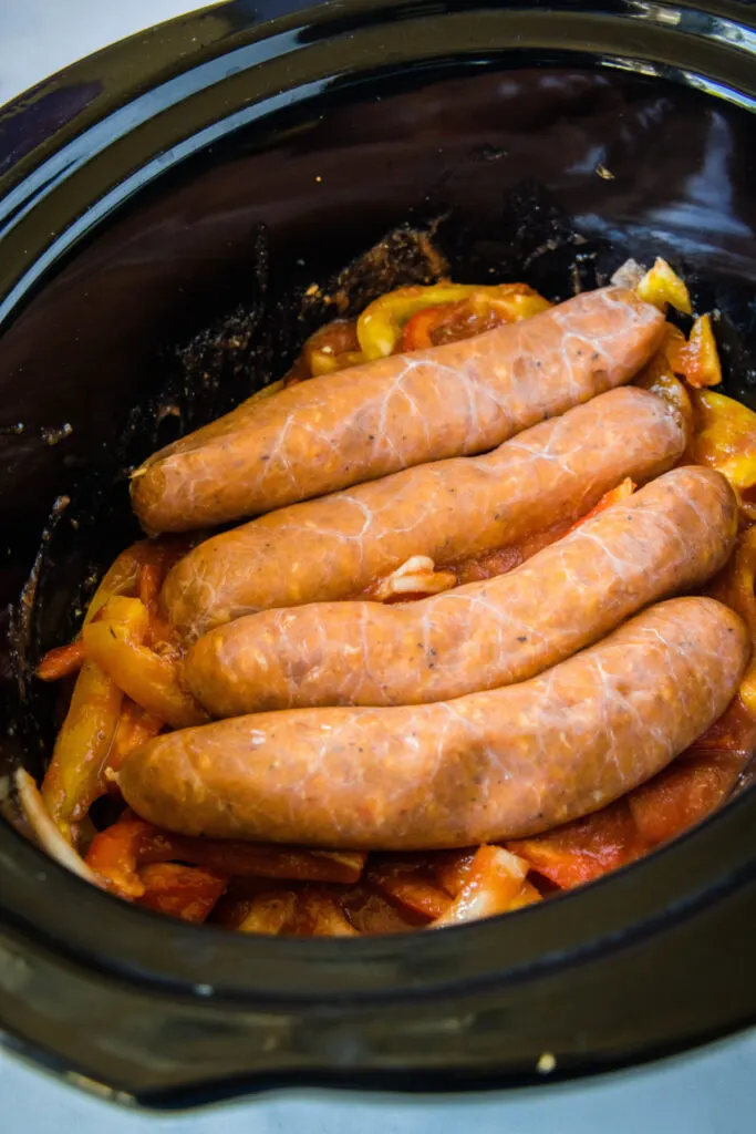Four sausages on top of a bed of peppers and onions in a crock pot
