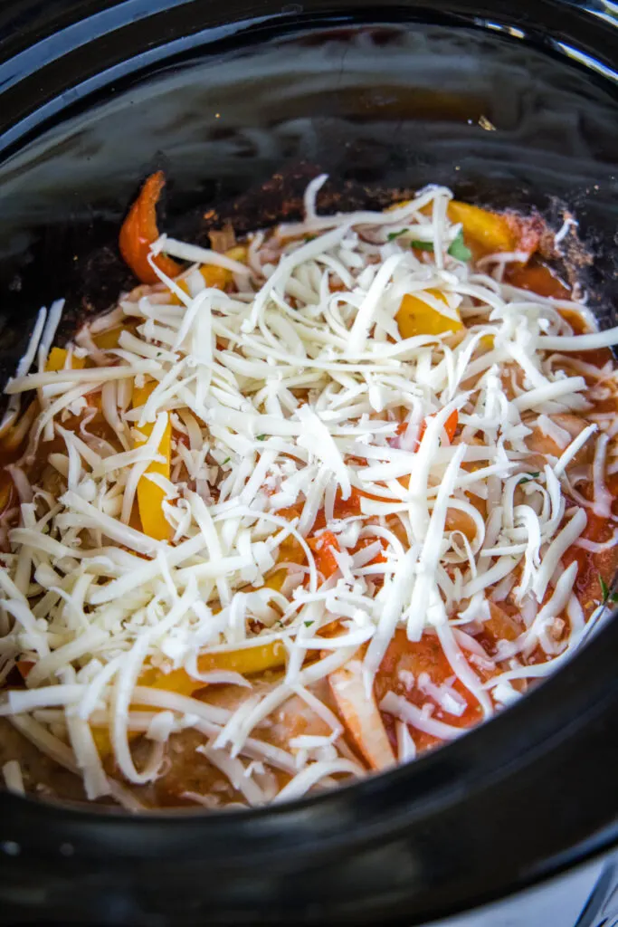 Shredded cheese on top of sausage and peppers in a slow cooker