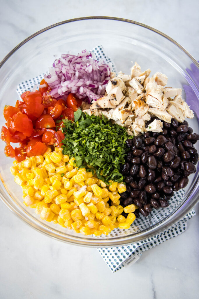 Overhead view of a mixing bowl filled with corn, tomatoes, onions, black beans, cilantro, and shredded chicken