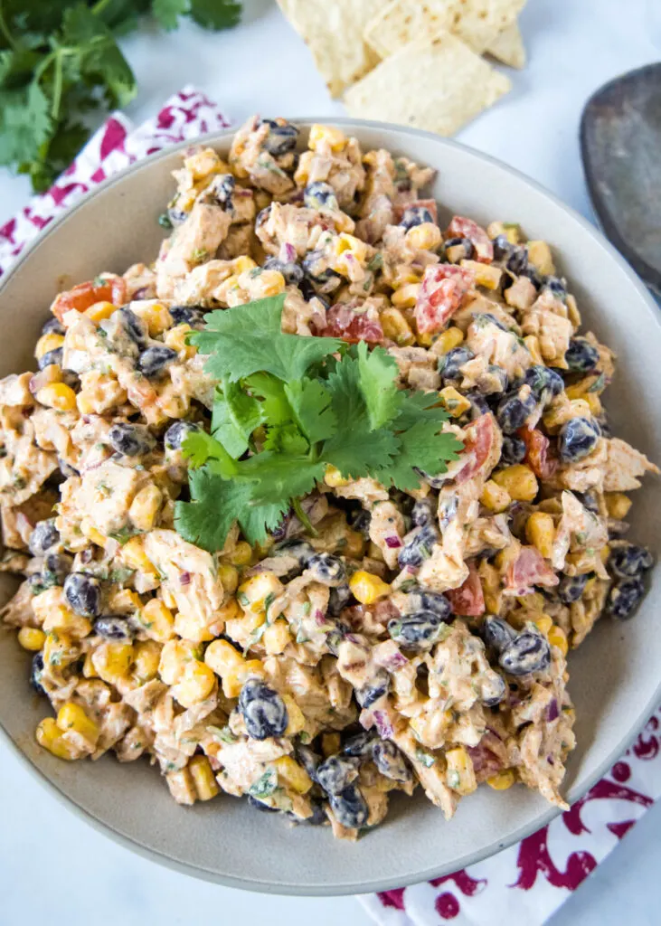 Overhead view of a bowl of chicken salad with tomatoes, corn, and beans, topped with cilantro
