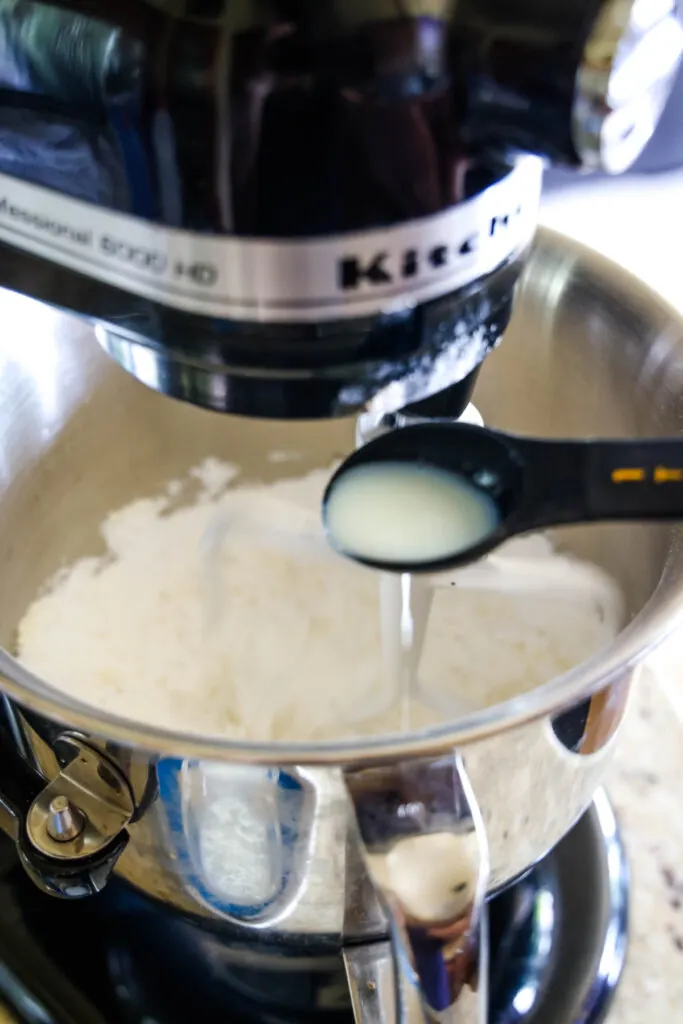 A teaspoon pouring milk into a stand mixer bowl with frosting