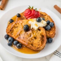 cropped close up air fryer french toast on a white plate with syrup and berries