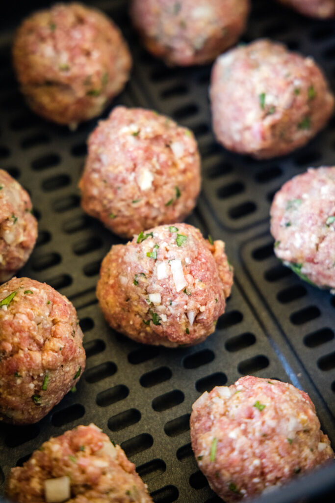 Close up of raw meatballs in an air fryer basket