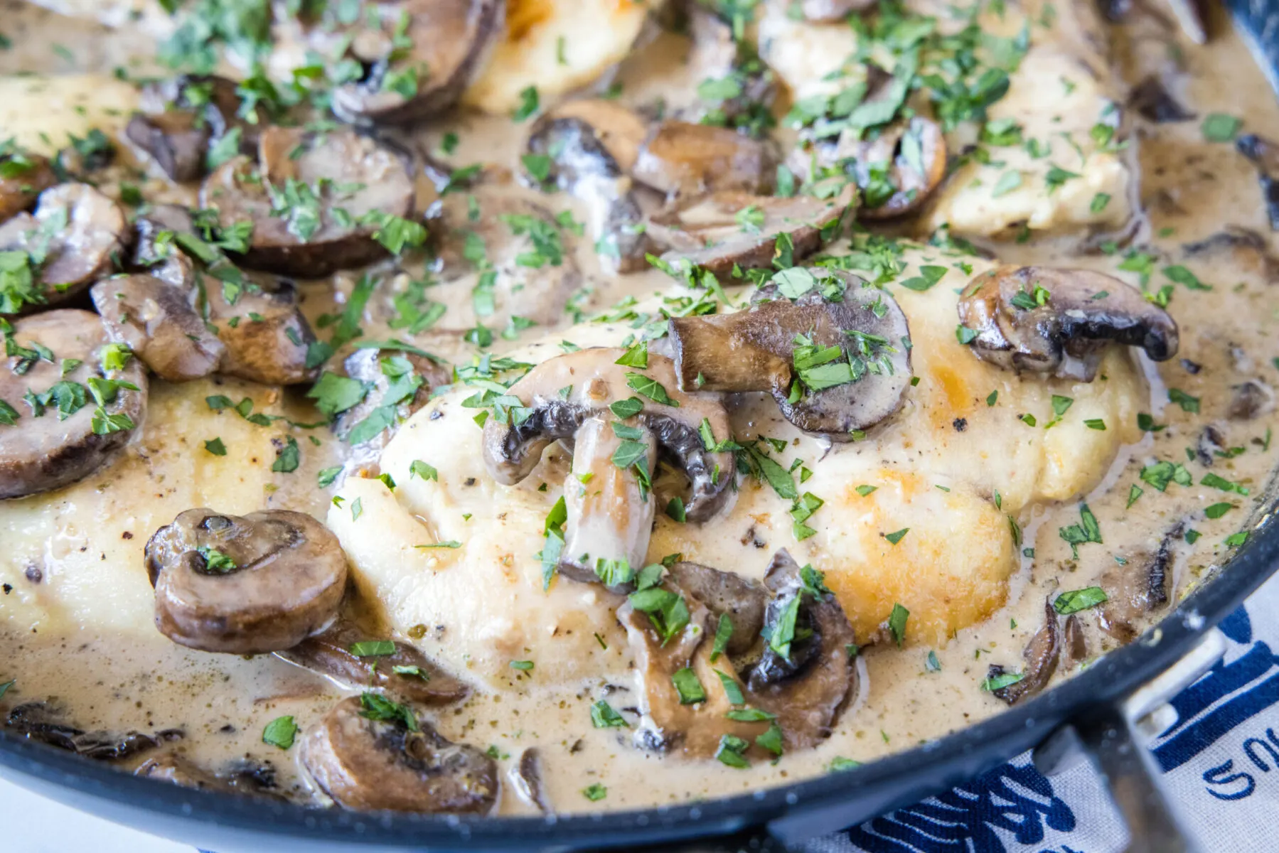 Close up of a chicken breast in a skillet covered in mushrooms, parsley, and sauce