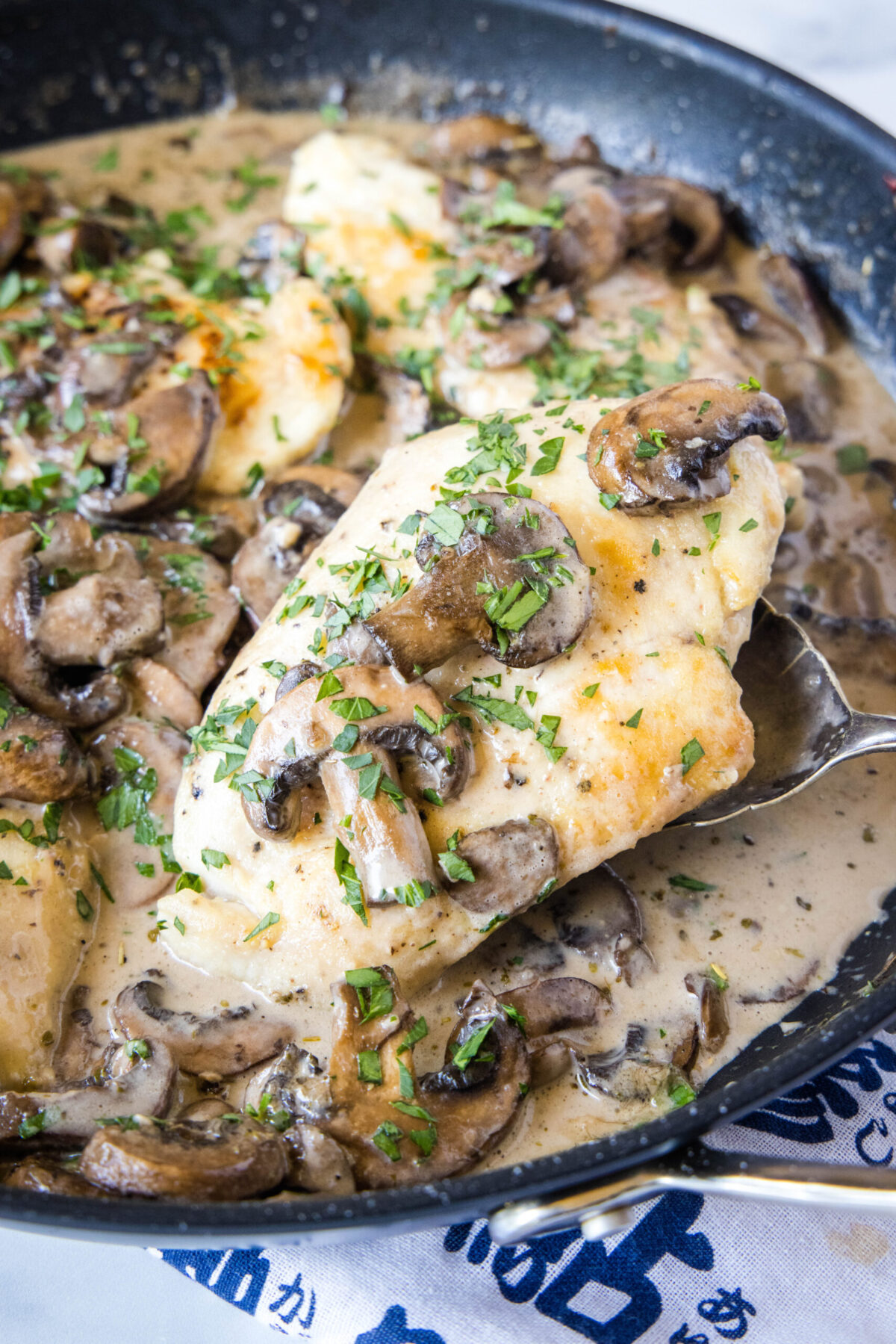 A spoon scooping out a chicken breast from a skillet of mushroom chicken