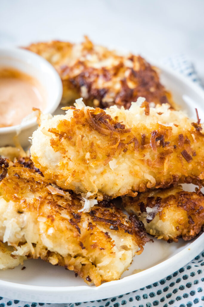 a white plate stacked with coconut crusted chicken tenders