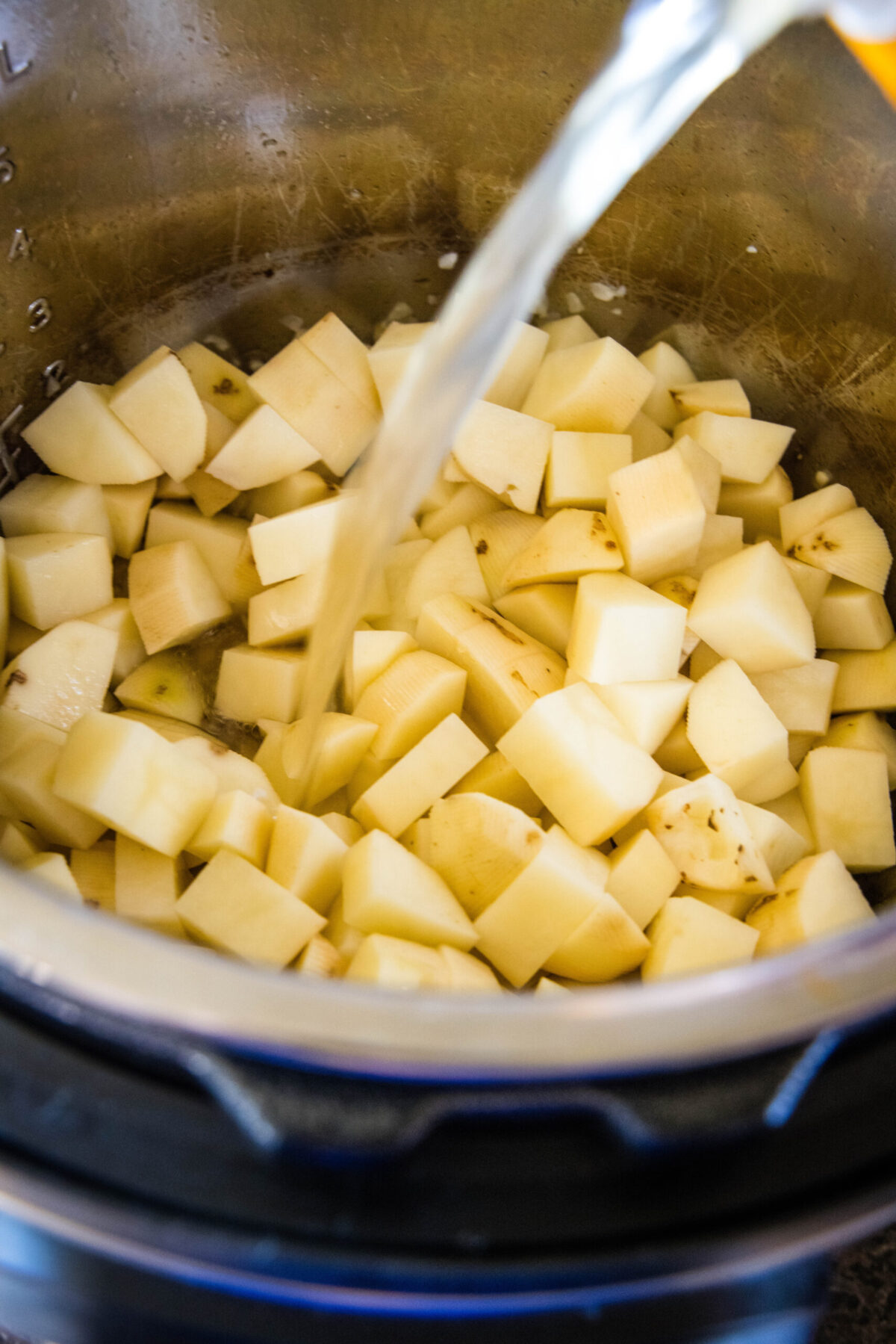 Chicken broth being poured over diced potatoes in a pot.