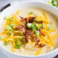 Close up of a bowl of potato soup with cheese, bacon, and green onions on top.