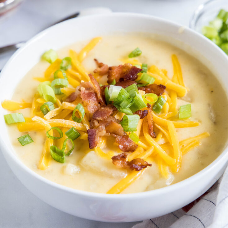 Close up of a bowl of potato soup topped with cheese, green onions, and bacon.