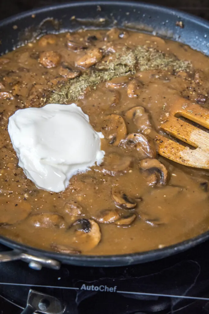 Mushroom stroganoff with a blob of sour cream on it, in a skillet, with a wooden spoon