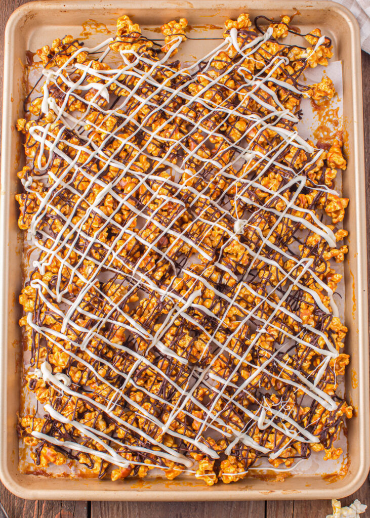 white chocolate and chocolate drizzled over caramel popcorn on a baking tray